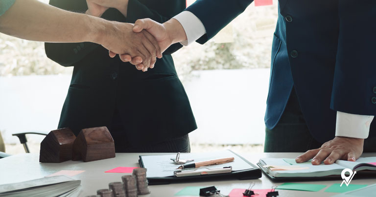 Two people shaking hands over a desk with documents
