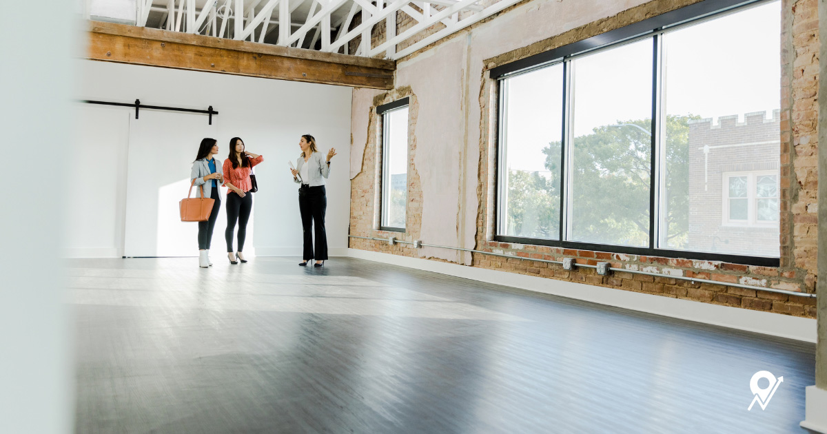 Three people touring an empty commercial space with large windows